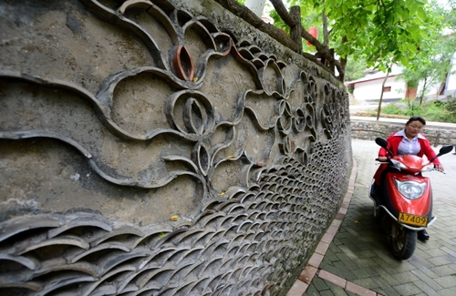 5月27日，在甘肃省陇南市康县王坝乡大水沟村，一名村民驾车从用废旧瓦片装饰的花坛旁走过。