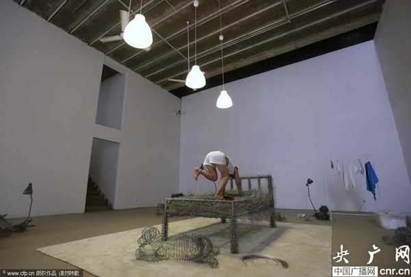 　2014年8月11日，北京，中国女艺术家周洁在北京现在画廊的展厅睡在一个未完成的铁丝床上，这一艺术项目被命名为“36天”，而这36天里，她可以正常进食、洗漱、如厕，以及玩手机等。