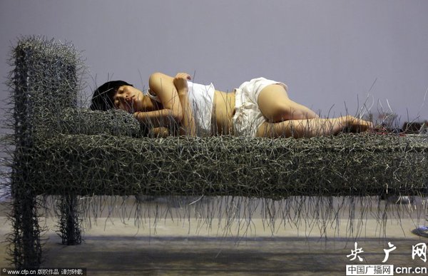 2014年8月11日，北京，中国女艺术家周洁在北京现在画廊的展厅睡在一个未完成的铁丝床上，这一艺术项目被命名为“36天”，而这36天里，她可以正常进食、洗漱、如厕，以及玩手机等。