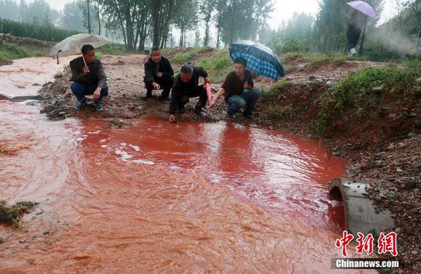 2014年9月15日，河南洛阳汝阳县马兰河因为污染变成一条“红河”，“红水”顺着山坡一直流到山下，而“红水”的源头正是附近一山顶的染料厂残留处理池。图为管道里冒出的红色污水与山上流下的雨水泾渭分明地流入马兰河。