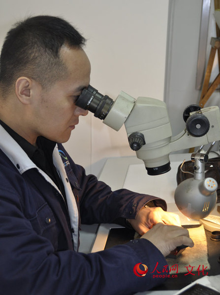 雕刻师正通过高倍放大镜，手持刀具在一块小小的钢版上，用手工雕刻出与邮票票面同样大小的部分图案。（人民网 王鹤瑾 摄）