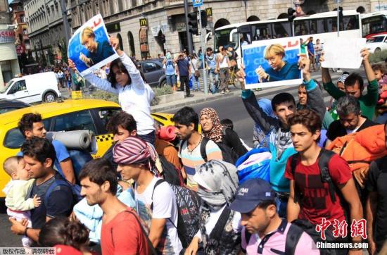 资料图：难民们手持默克尔的照片，从匈牙利步行前往奥地利。