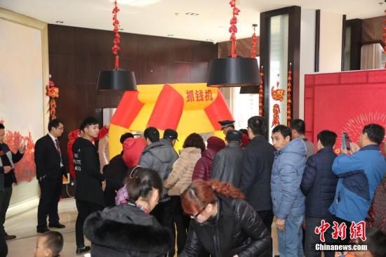 资料图：2016年2月27日，山东东营，看房的市民在商家设置的“抢钱机”内抢着飞舞的人民币，抢到的人民币归市民所有。由于房地产市场低迷，山东东营的某楼盘为了吸引前来看房的市民，在售楼处安装了“抢钱机”，看房的市民排成长队“抢钱”，用真金白银刺激看房客。 图片来源：视觉中国
