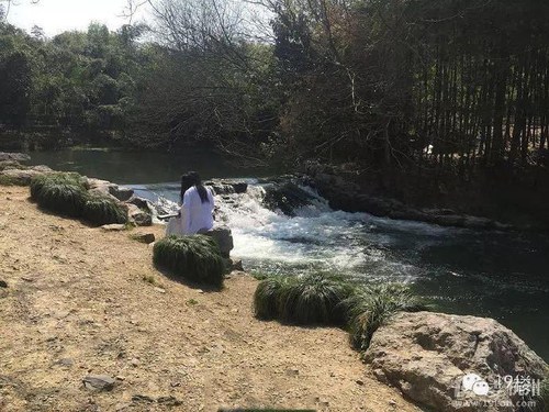 图为一白衣长发人坐水边抚琴。