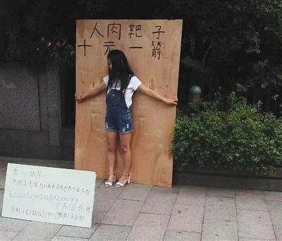 　杭州武林广场一女孩站在一块大木板前头，木板上写有“人肉靶子，十元一箭”字样。