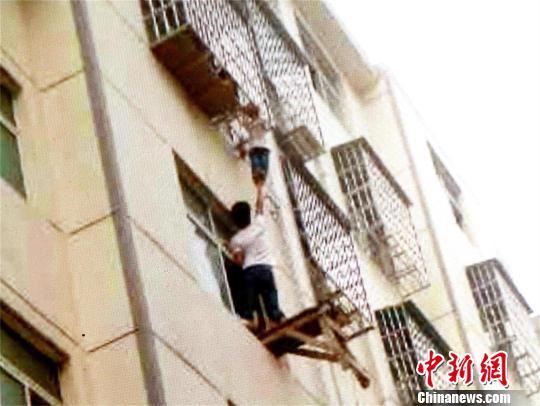 一业主左手抓住窗户边沿，右手托举男孩双脚 宋俊初 摄