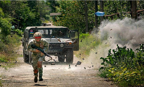 图为乌政府军的悍马军车遭到伏击，附近发生爆炸，沙石乱溅，一只塑料瓶凌空飞起，一名乌军士兵在前方躲避敌方火力。