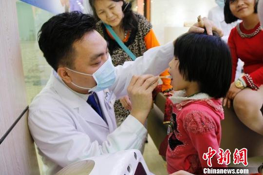 张菲(左2)看着孩子接受免费的口腔检查?！⌒そ?摄