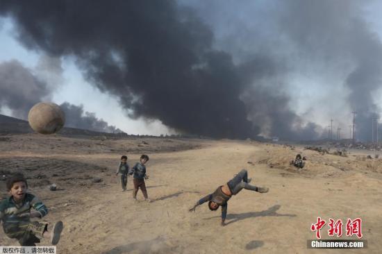 苦中作乐是孩子们的宝贵技能，大人们会逐渐被现实的痛苦和窘境压倒，失去追求快乐的能力，但孩子们不会。他们永远能在艰苦的条件下获得快乐，因为他们追求的快乐非常简单。图为当地时间2016年11月23日，伊拉克摩苏尔，极端分子在逃离Al Qayyarah小镇前点燃油井，几名儿童在滚滚浓烟中踢球。