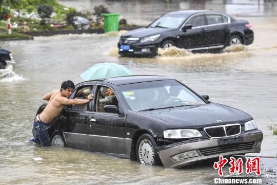6月13日，惠州惠东县新平大道上，市民在雨中推行抛锚的车辆。　陈骥旻 摄