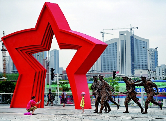 南昌，人民军队诞生的地方。在这座有着“英雄城”美誉的城市街头，以“八一”命名的地方随处可见：八一广场、八一公园、八一大道、八一起义纪念碑……这一切，都源于90年前8月1日发生在这里的一次影响深远的武装起义。八一南昌起义，让南昌这个军旗升起的地方烙上了深深的红色印记。图为在南昌建军雕塑广场，一位家长在给孩子拍照。    新华社发