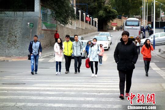 图为市民们穿着棉服、羽绒服在寒风中卷缩着过马路?！∷镱?摄