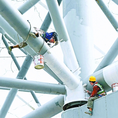 粗壮的钢结构犹如大树的主干和次干，枝繁叶茂，富有活力。工人师傅们正在滚涂防火涂料。