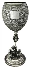 征战图高脚杯   Standing Trophy with Battle Scene Pattern 晚清 通高：29cm；口径：9.5cm；底径：10.6cm；重:681g 款识：慎昌，LW   清代中晚期，随着外销银器的逐渐升温，银匠不仅开始借鉴青铜器、瓷器的特征创造银器，更融合进宗教思想及丰富的想象力。征战图高脚杯的杯身运用锤揲工艺由内向外敲击出隋唐故事“罗通扫北”浮雕图，在杯身中央位置留有一醒目光面盾牌，用以錾刻购买者家族族徽，一方面彰显其身份地位，另一方面也能够起到防盗的作用。整体造型极具艺术感，杯托被设计成一只展翅翱翔的雄鹰，杯杆被设计成配有圆环的锡杖造型。底座焊接一打坐罗汉和一伏虎抱杵罗汉，底座整体设计成须弥山的造型，须弥山在印度佛教中象征着世界之中心，整体做工精湛，布局巧妙，体现了银匠的艺术造诣与佛教思想的融合。