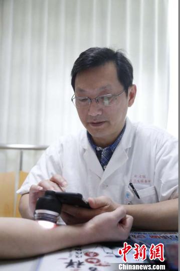 蔡医生用手持式皮肤镜给患者身上的一处“色斑”拍摄照片，然后上传到手机上一款应用程序(APP)中。　芊烨 摄