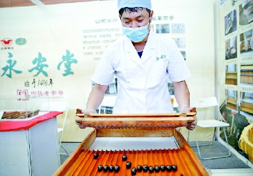 ▲图为工作人员在活动现场向观众展示中药蜜丸制作工艺。