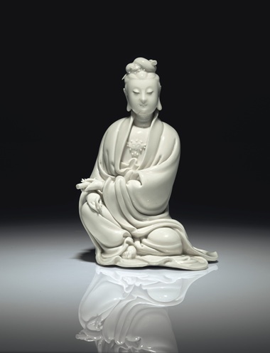 明十七世纪初 德化白釉书卷观音坐像 《何朝宗》葫芦形印款，高8 58 寸 (21.9公分)。估价：60,000-80,000美元。此拍品于2018年9月13至14日在佳士得纽约亚洲艺术周之中国瓷器及工艺精品拍卖中呈献。