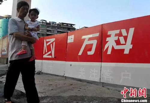 资料图：福州民众从万科楼盘工地旁经过。<a target='_blank' href='http://www.chinanews.com/'>中新社</a>记者 张斌 摄