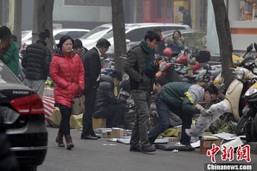 一家快递公司的员工蹲在马路边分发邮件，身边堆放着大量的包裹。 王中举 摄
