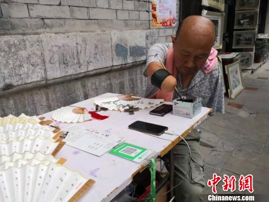 贾维军坐在自己的简易摊位前写字?！“⒘漳?摄