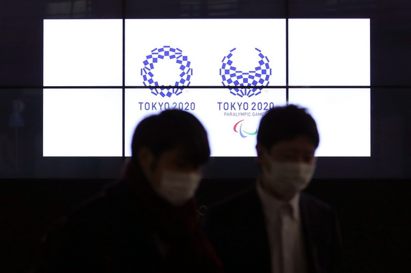 3月30日，在日本东京新桥，行人经过显示东京奥运会和残奥会会徽的电子屏。